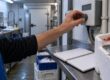 Arrière-boutique alimentaire où une main règle le boîtier de contrôle d'une chambre froide près d'un carnet de relevés de température.